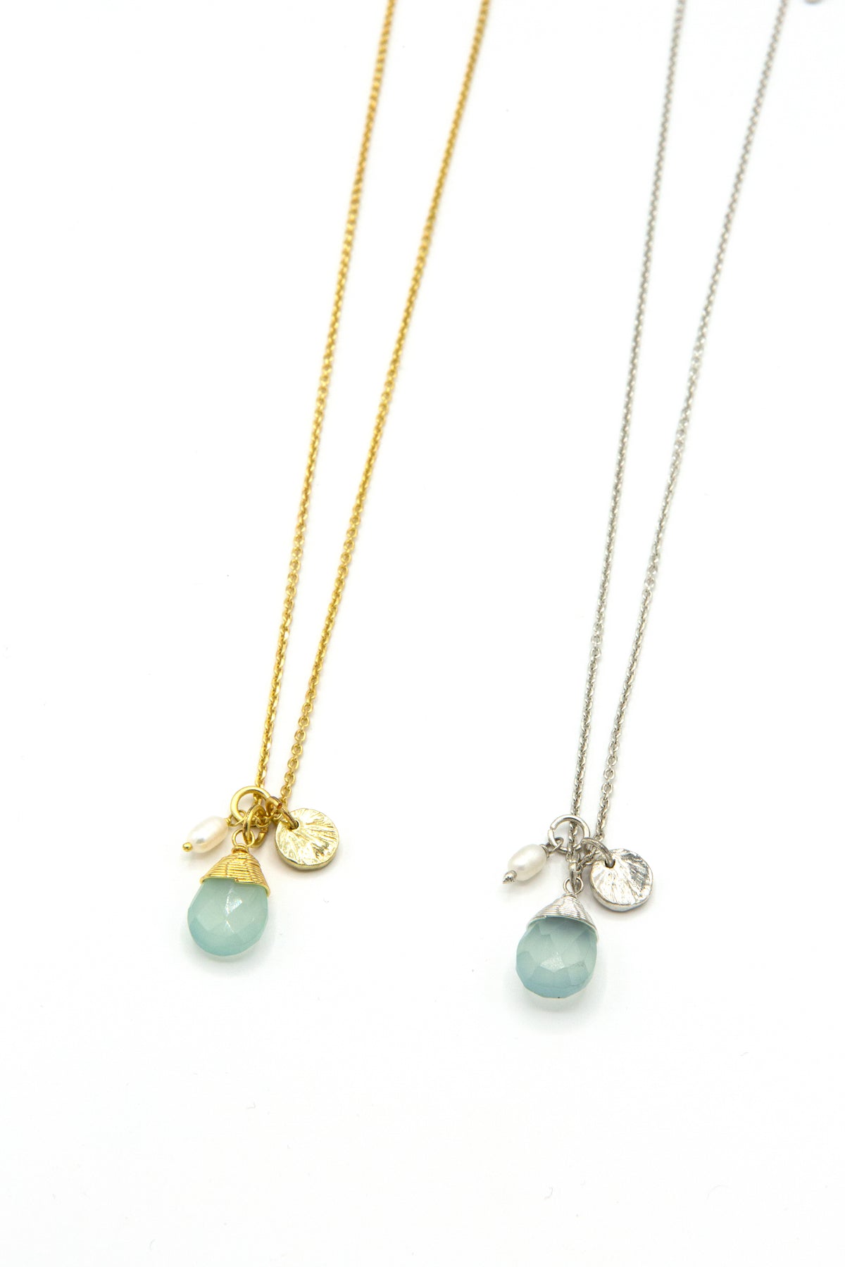 Pair of Fair Anita Tiny Treasures charm necklaces shown in gold and silver finishes, featuring aqua chalcedony teardrop pendants, freshwater pearls, and textured charms.