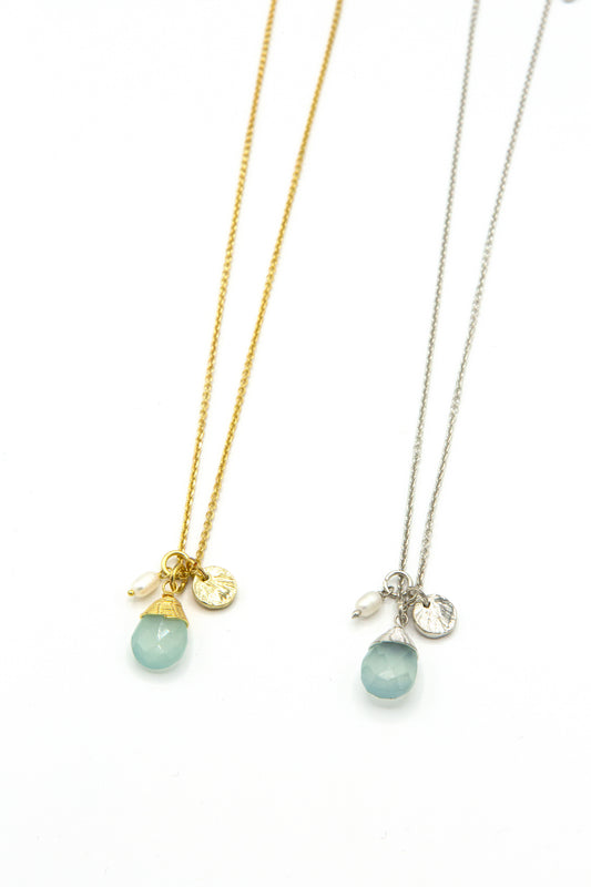 Pair of Fair Anita Tiny Treasures charm necklaces shown in gold and silver finishes, featuring aqua chalcedony teardrop pendants, freshwater pearls, and textured charms.